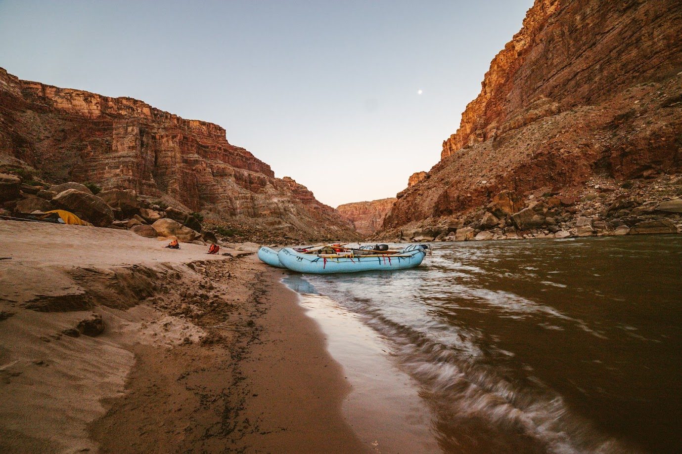 Rafts beached at a river camp beneath canyon walls at dusk